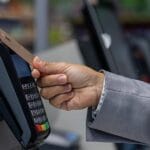 A person uses a contactless payment card at a point-of-sale terminal, highlighting reliance on cloud-first POS systems for transactions.